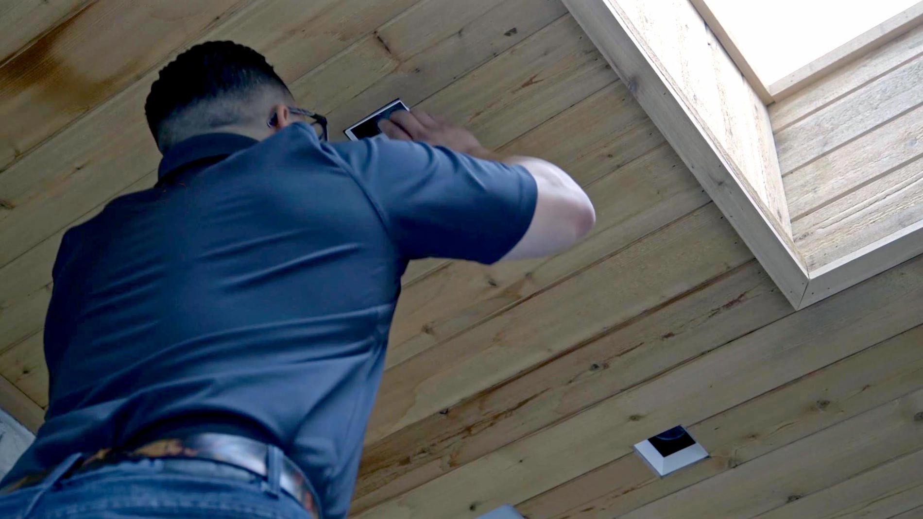 Technician installing a square recessed speaker into a wood plank ceiling