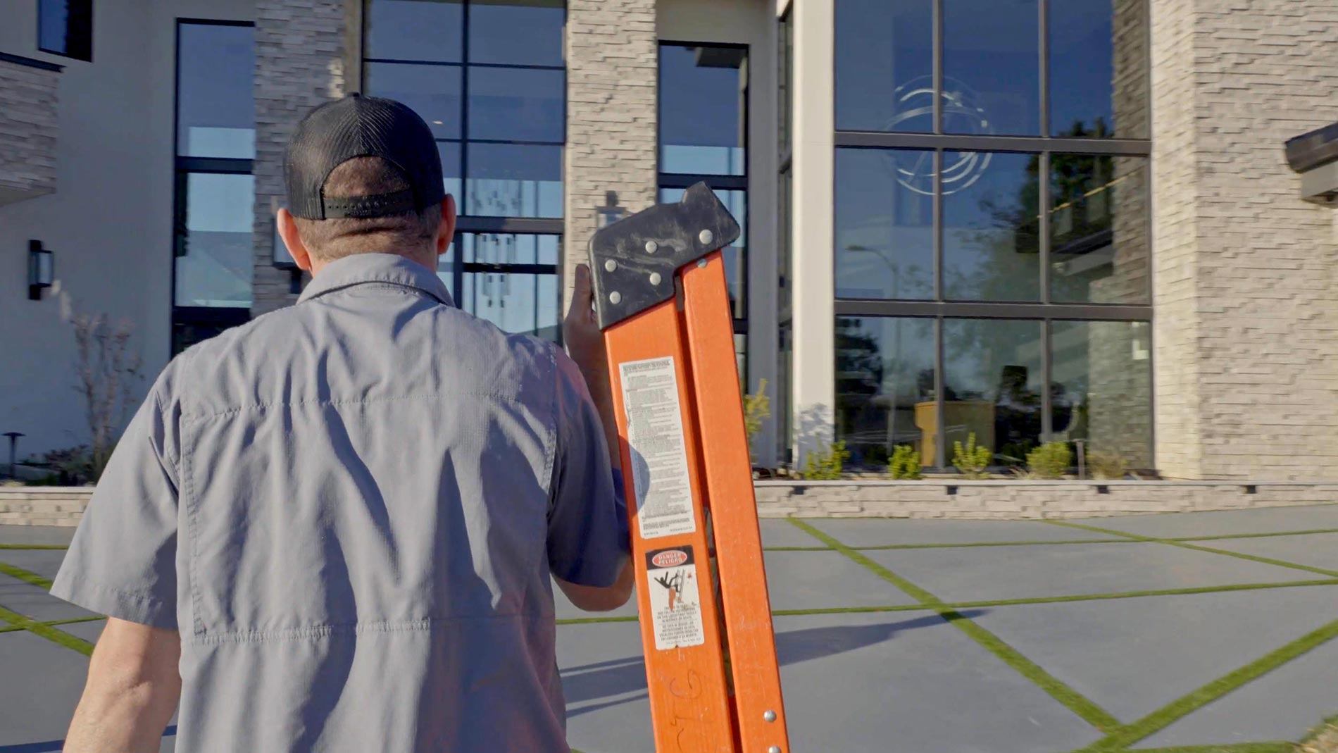 Technician carrying an orange ladder toward a large glass building
