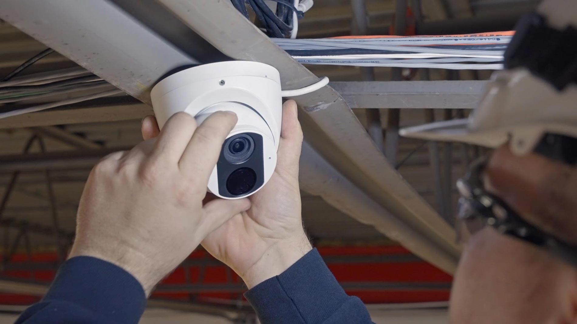 Technician mounting a white dome security camera to a ceiling beam